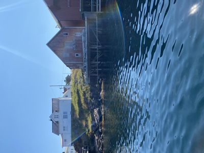 Fotografi av en bygning (trollfiskehus) ved vannkanten, sett fra vannet.