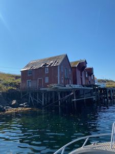 Fotografi av en rød trebygning (trollkari) på stolper ved vannet, sett fra en båt.