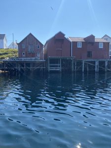 Fotografi av røde stuehus bygget på stolper over vannet, sannsynligvis i en kystby.