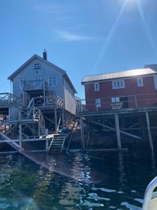 Fotografi av to hytter eller båthytter på stolper i vannet, sett fra en båt.