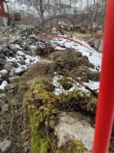 Fotografi av en byggeplass med stein, snø, og deler av en bygning i bakgrunnen.