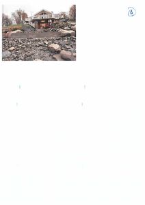 Fotografi av en bygning på en bratt tomt med stein og grus i forgrunnen.