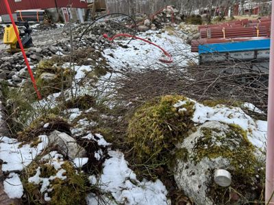 Fotografi av et byggeplassområde med snø, grener og byggematerialer.