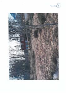 Fotografi av en rød bygning sett fra siden, med skog og terreng i forgrunnen.