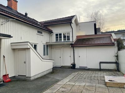 Fotografi av en hvit, toetasjes bolig med garasje og trapp opp til etasjen.