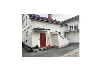 Fotografi av fasaden på en hvit, trepanelert bolig med rød inngangsdør og garasjeport.