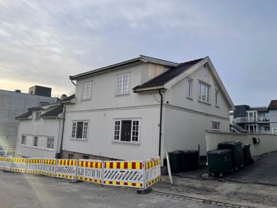 Fotografi av en nybygd eller renovert villa med hvite fasader, sett fra gaten med en gjerde i forgrunnen.