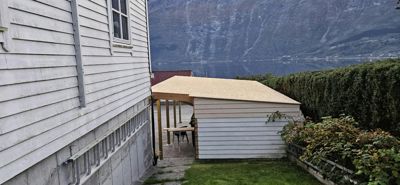 Fotografi av en nybygd eller ombygd bygning (trollhytte) i en bakgård med fjell og vann i bakgrunnen.