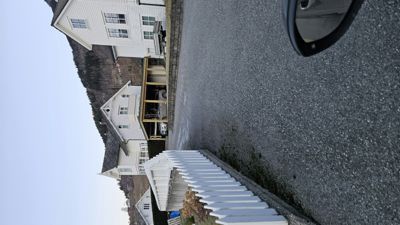 Fotografi av en hvit villa med garasje og hage, sett fra en vei.