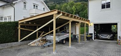 Fotografi av en ferdig eller nesten ferdig bygget trekonstruksjon (kariport/veranda) i bakgården til en bolig.