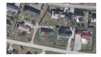 Flyfoto eller satellittbilde av et boligområde med en markert eiendom (rød pinne) og grønn kryssmarkering for byggefelt.