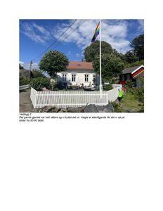 Fotografi av en hvit villa med stakittgjerde, flaggstang og omgivelser.