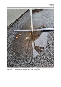 Fotografi av skader i asfalt med vannoppsamling og en målebånd for dokumentasjon.