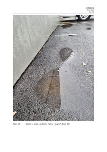Fotografi som viser skader i asfalt ved en betongvegg, med bildebeskrivelse 'Skader i asfalt, sydvestre hjørne bygg D'.