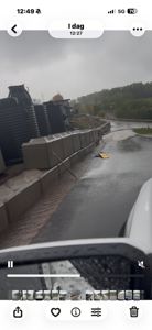 Fotografi av en vei som er oversvømt med brun vann, med store svarte siloer eller containere til venstre og en betongmur langs veien.