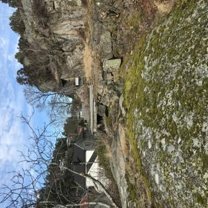 Fotografi av en bygning (hus) sett fra en vinkel med stein og vegetasjon i forgrunnen.