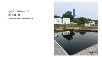 Fotografi av eiendom (Fjellknausen) sett fra vannet, med en blå pil som peker ut bygningen.