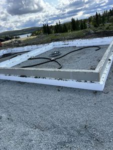 Fotografi av en ferdigstilt betongfundament med hvit maling og grusdekke på et byggeplass.