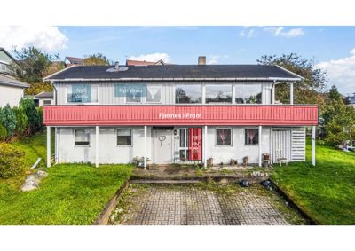 Fotografi av en eksisterende toetasjes bolig med tilhørende hage og kjelleråpning.