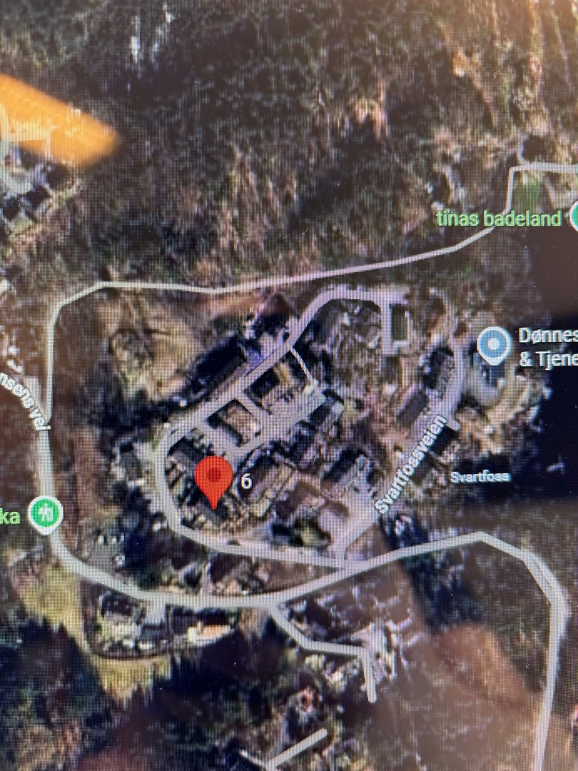 Satellittbilde eller kartutsnitt som viser en bebygd område med veier, eiendommer og grøntområder. Det er merket med en rød pinne og tekst som 'Svartfossveien' og 'Dønnes & Tjernes'.