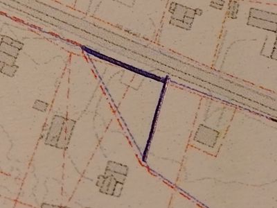 Et detaljutsnitt fra en situasjonsplan som viser eiendomsgrenser (tomtegrenser) og en vei. Det er tegnet inn en ny grense med blå penn.