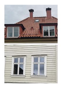 Fotografi av en bygning som viser taket med rødt taktegl, to skorsteiner og et vinduslyst, samt fasaden med hvite vinduer og horisontale trepanel.