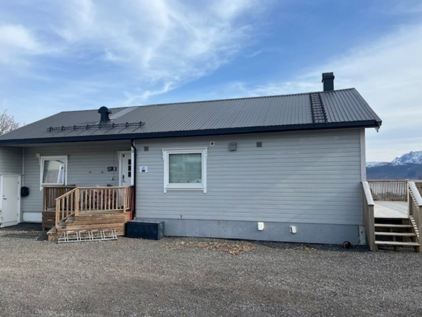 Fotografi av en grå enebolig sett fra siden, med tak, vinduer, dører og trapper synlig.