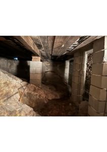 Fotografi av en underjordisk eller krawellertomte med blokkvegger, betongbjelker og rørgjennomføringer.