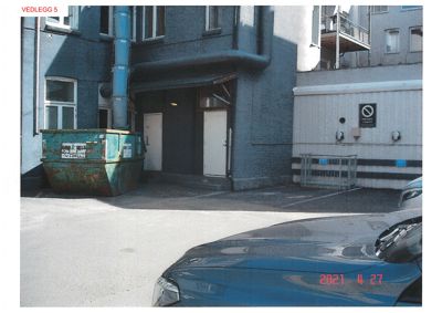 Fotografi av en bygning med en container og en bil i forgrunnen.