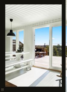 Fotografi av et interiør (spisestue) med hvite panelvegger, gulv og tak, samt store glasdører som åpner ut til en terrasse.