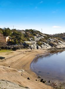Fotografi av en kyststrøk med en liten gul hytte på en klipperik bakke.