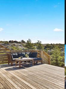 Fotografi av en uteplass med treterrasse, møbler og utsikt over et naturområde.