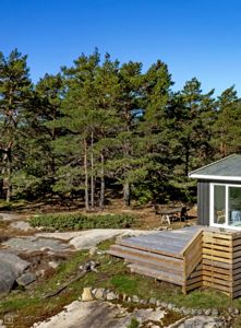 Fotografi av en hytte med terrasse og omgivelser i skogen.