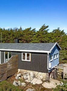 Fotografi av en eksisterende hytte sett fra siden, med synlig fasade, tak og omgivelser.