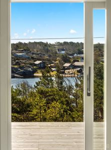 Fotografi som viser utsikt fra en terrasse eller balkong mot et kystlandskap med hus, vann og trær.