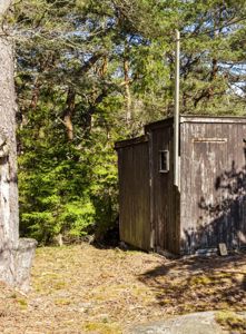 Fotografi av en liten, mørk trehytte eller uthus plassert i en skog.