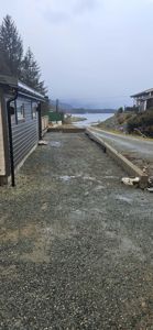 Fotografi av en byggeplass med en ferdig fasade på venstre side, en nybygd betongmur i forgrunnen og utsikt over vann og fjell i bakgrunnen.