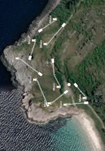Satellittbilde av en kystlinje med overlagte ruter som viser antatte posisjoner for bygninger (merket 'Main') og tilhørende veier eller tilknytninger.