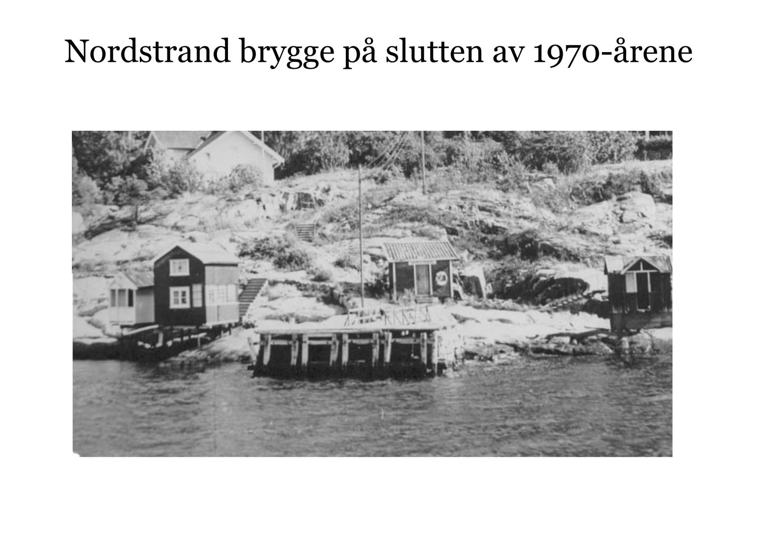 Et svart-hvitt fotografi av Nordstrand brygge på slutten av 1970-årene, som viser små hytter og en brygge ved kysten.