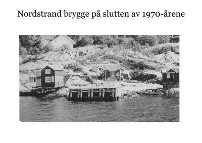 Et svart-hvitt fotografi av Nordstrand brygge på slutten av 1970-årene, som viser små hytter og en brygge ved kysten.
