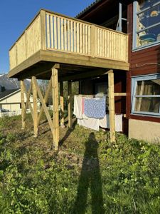 Fotografi av en ferdig eller nesten ferdig utbygd terrasse med støtter og rister, festet til en bolig.