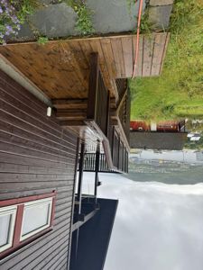 Fotografi av en utvendig trapp og terrasse ved siden av en mørk trehytte, med utsikt over vann og fjell i bakgrunnen.