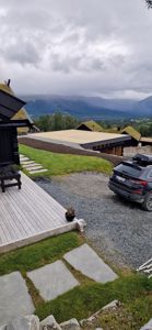 Fotografi av en moderne bygning med grønt tak, sett fra utsiden mot bakgrunn av fjell og skyer.