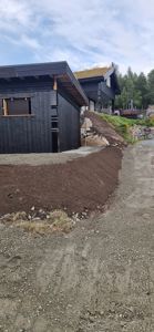 Fotografi av en nybygd eller under oppussing bygning med mørk fasade og grønt tak, sett fra bakkenivå.