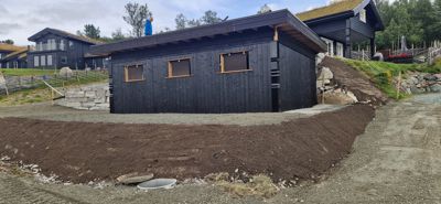 Fotografi av en nybygd eller under oppussing hvitkalket/gravert hytte med mørke fasader, sett fra siden.