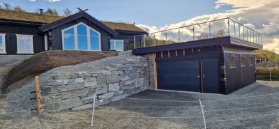 Fotografi av en moderne bolig med grønt tak, garasje og steinmur under bygging.