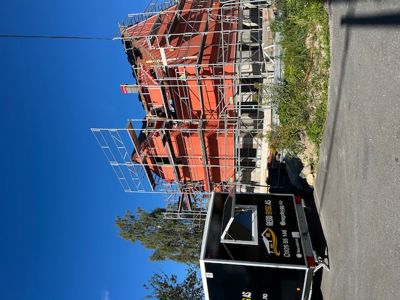 Fotografi av en bygning under oppføring med rødt treverk og stålkonstruksjon, omgitt av stålrekkverk og en lastebil.