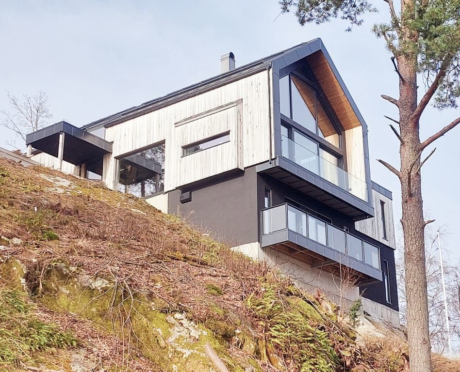 Fotografi av en moderne villa sett fra siden, plassert på en skråning.