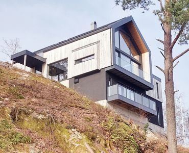 Fotografi av en moderne villa sett fra siden, plassert på en skråning.